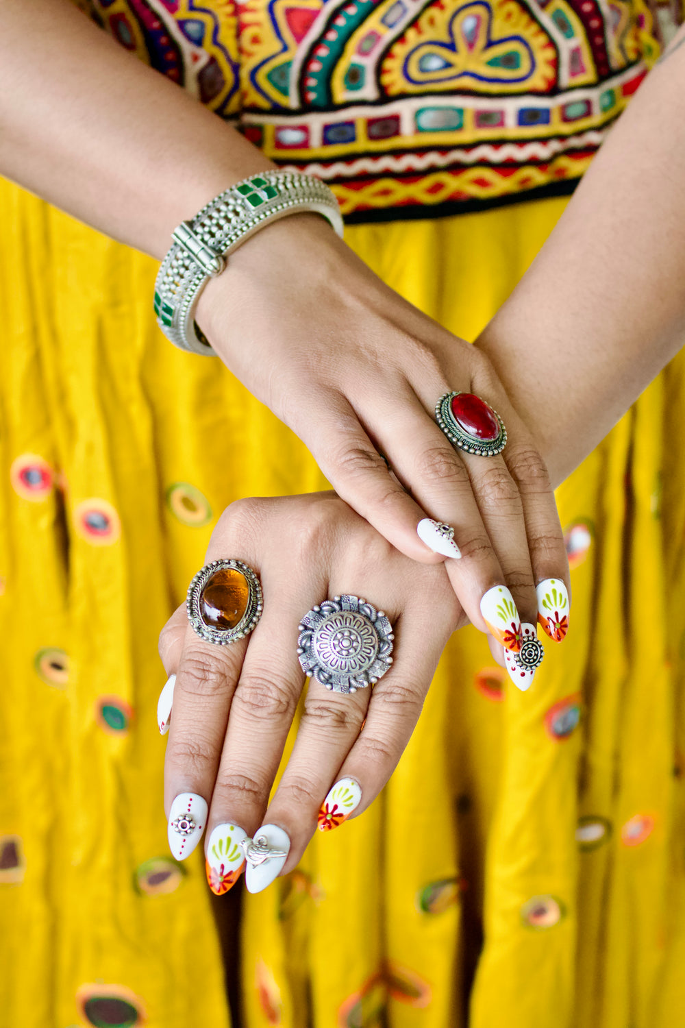 Raas Rani press-on nails with oxidised silver rings and bangles, hands crossed against a yellow Navratri skirt