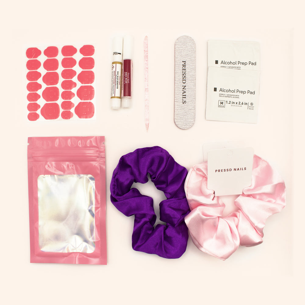 Complete Pressd Nails toolkit with adhesive tabs, nail glue, nail glue remover, nail file, cuticle pusher, alcohol prep pads, pink pouch, and pink and purple scrunchies